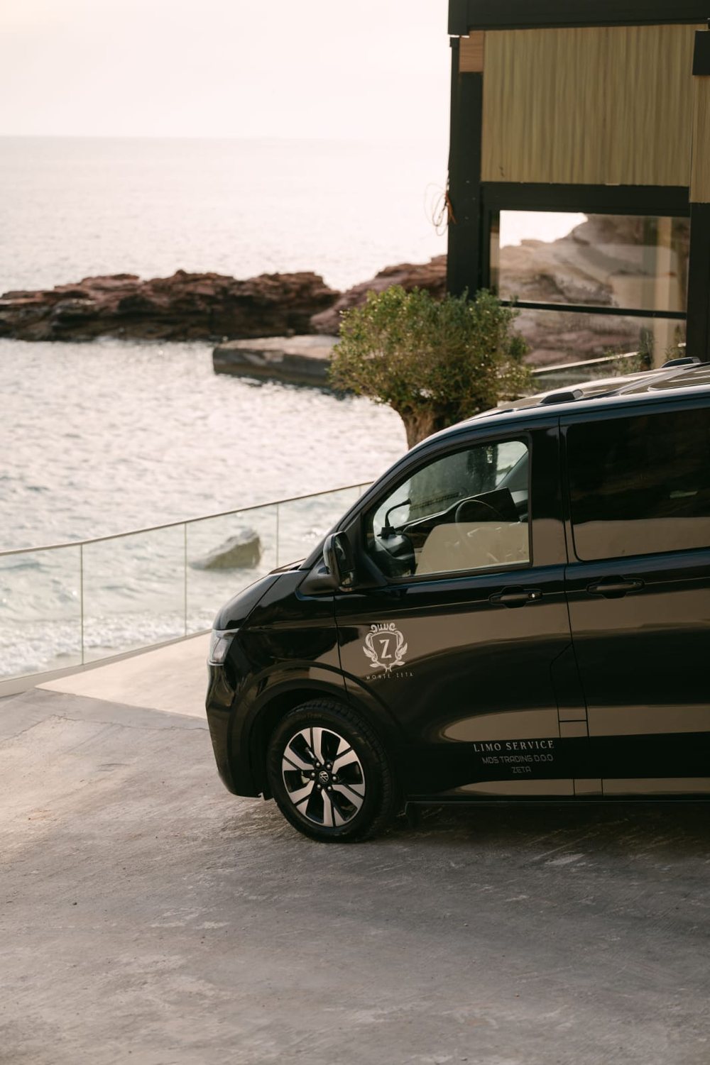 Two black vans of the Monte Zeta fleet parked side by side beside a stone wall